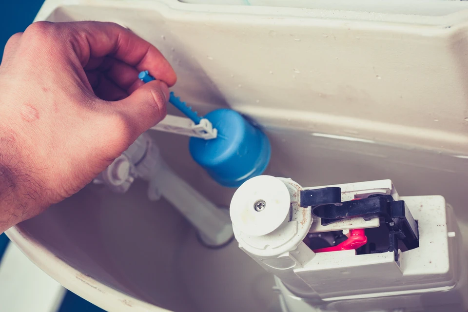 Une main actionne la poignée chromée d'une chasse d'eau de toilettes dans un environnement sanitaire blanc et épuré