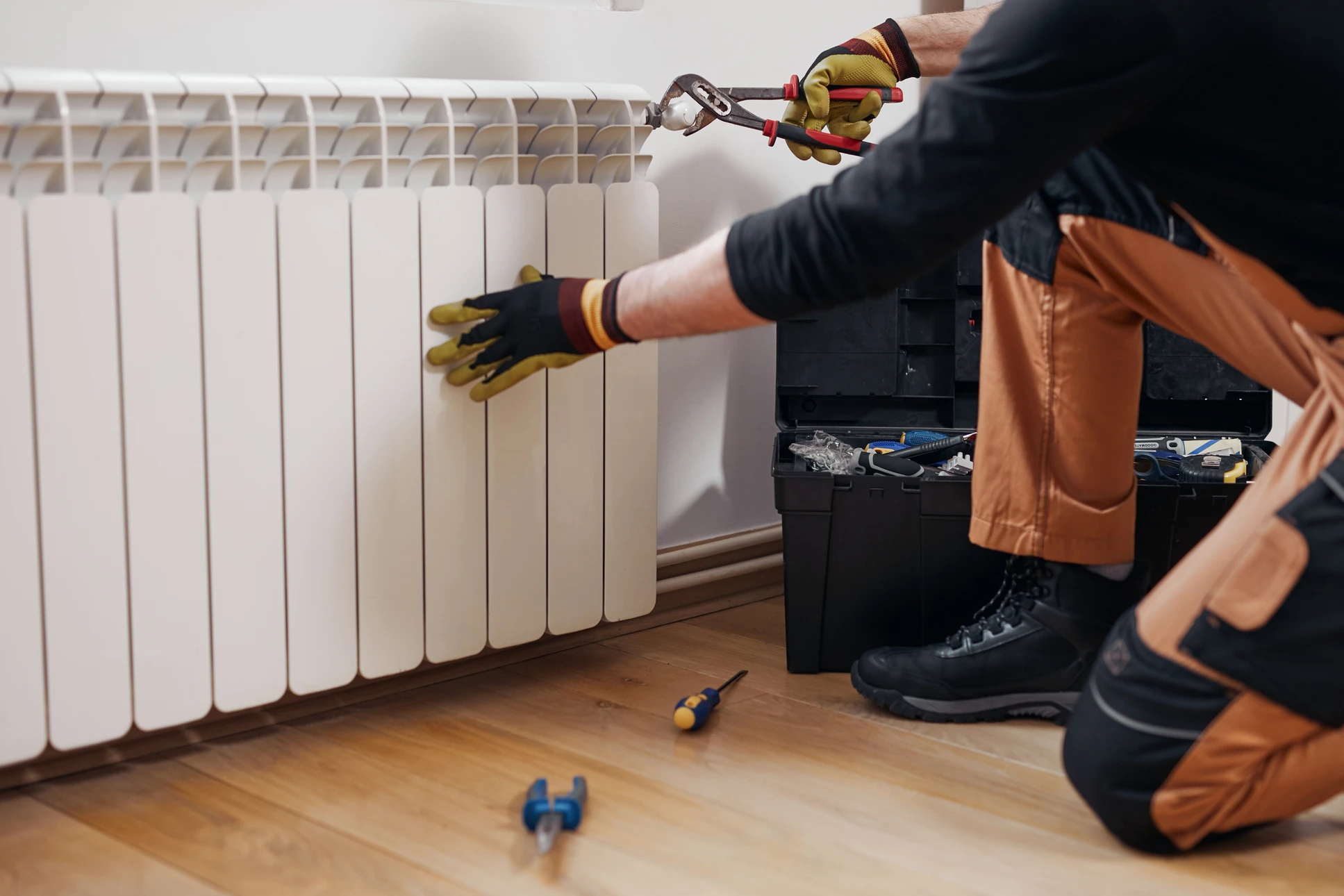 Plombier en salopette bleue travaillant à genoux dans salle de bain moderne, manipulant outils de plomberie