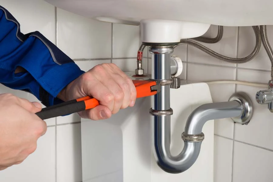 Main dans un gant de protection bleu nitrile pointant vers une fissure dans une baignoire blanche