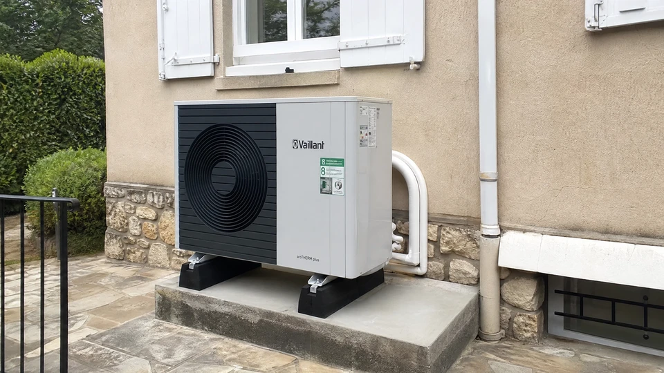 Un plombier en casque jaune installe un collecteur de chauffage au sol dans un local technique