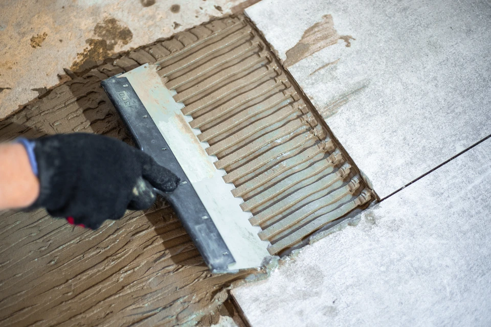 Ouvrier carreleur professionnel installant du carrelage dans une pièce en rénovation, utilisant une ventouse de pose pour positionner les carreaux blancs
